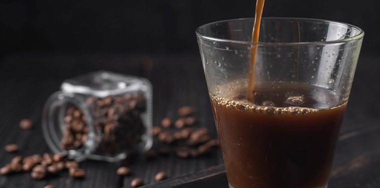 Tipos de café: café negro siendo vertido en vaso de vidrio desde una cafetera moka sobre mesa oscura. Café.